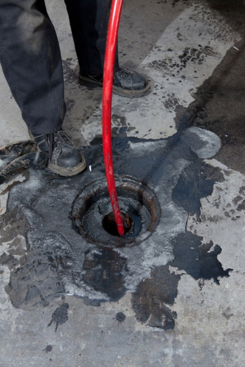 Untitled design (9) Commercial plumbers hydro line jet a pipe at a large restaurant. Grease can be seen on the pavement surrounding the pipe.