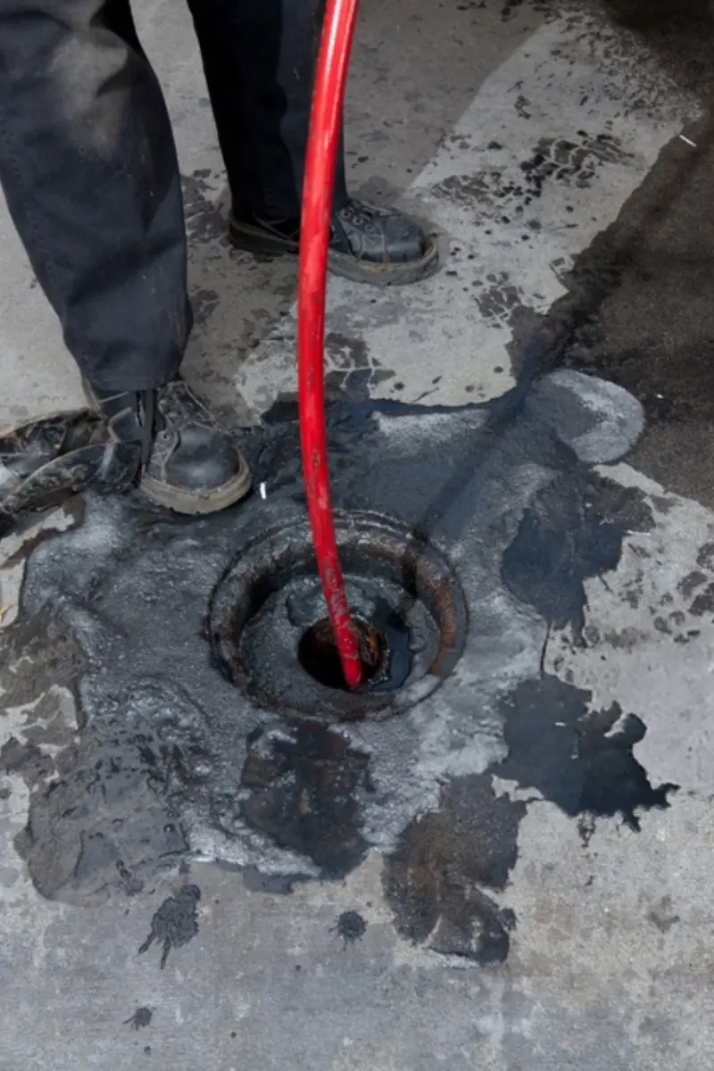 Untitled design (9) Commercial plumbers hydro line jet a pipe at a large restaurant. Grease can be seen on the pavement surrounding the pipe.